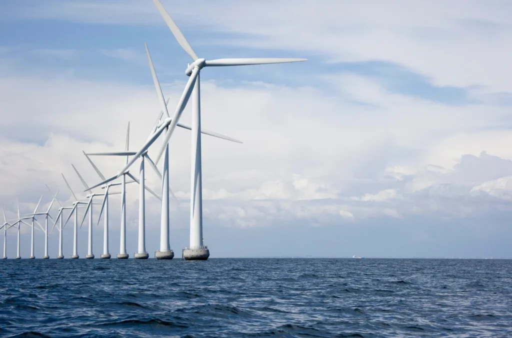 A row of offshore wind turbines stands in the sea beneath a partly cloudy sky, generating renewable energy. | Bentley Systems | Infrastructure Engineering Software Company A row of offshore wind turbines stands in the sea beneath a partly cloudy sky, generating renewable energy.