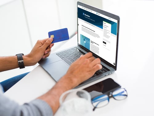 Person holding a credit card while using a laptop displaying a website, with a smartphone, glasses, and a pair of earphones on a white surface nearby. The setup captures the essence of modern infrastructure design for seamless online transactions. | Bentley Systems | Infrastructure Engineering Software Company Person holding a credit card while using a laptop displaying a website, with a smartphone, glasses, and a pair of earphones on a white surface nearby. The setup captures the essence of modern infrastructure design for seamless online transactions.