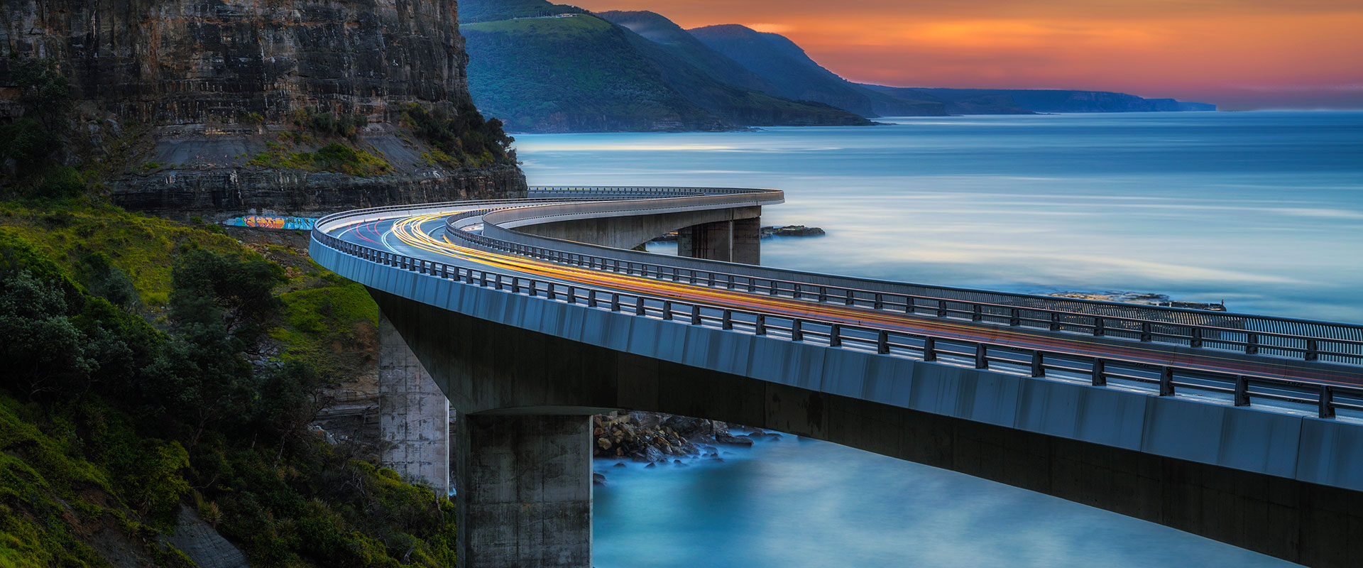 Sunset over the Sea cliff bridge along Australian Pacific ocean coast with lights of passing cars