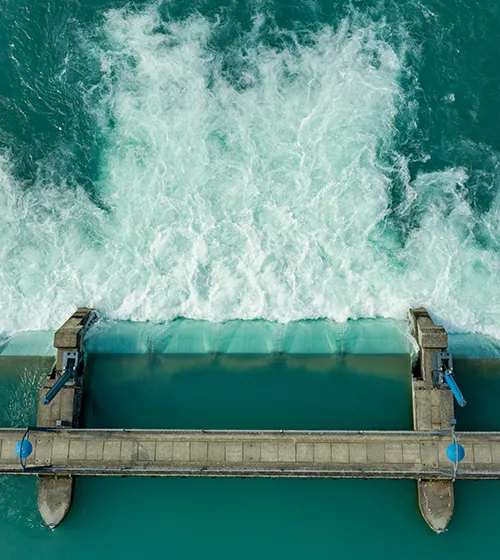 Aerial view of water rushing over a dam with a walkway and machinery on both sides.