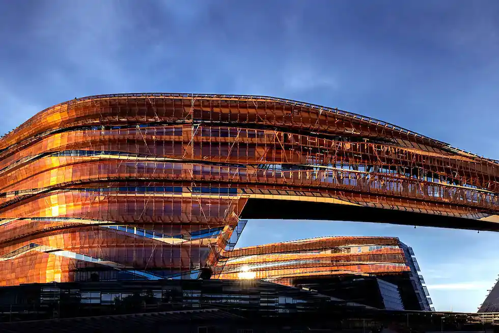 Modern building with curved, layered architecture and reflective copper-colored surfaces under a blue sky, showcasing product value with design as innovative as GA4's analytics.