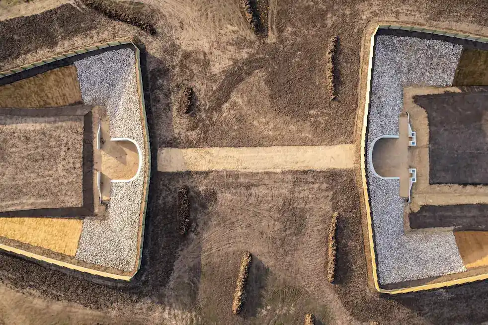 Aerial view of two symmetrical, fortified earth structures with gravel and dirt paths, separated by a central walkway on barren ground—showcasing technology innovation in modern landscape design.
